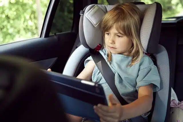little girl on seat belt at rear seat of car with tablet